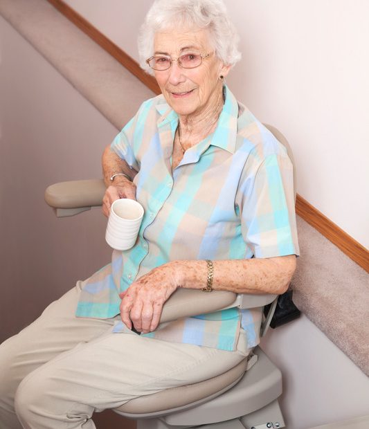 93 year old woman using preowned stairlift in her home, carrying her coffee downstairs.