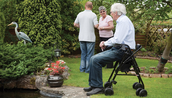 Uniscan Rollator in black being used as a seat while the gentleman enjoys a rest in the park